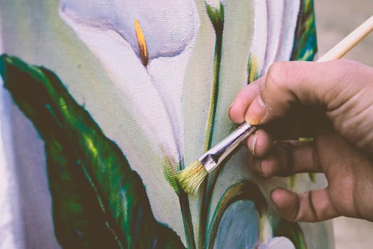 Close-up view of an artist painting a floral design on canvas using a brush.
